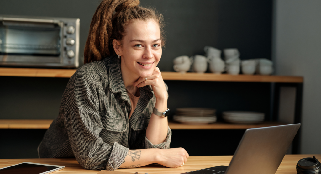 Business owner stood at a desk with a laptop with coffee cups in a cafe setting