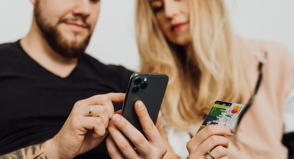 A man and woman sit next to each other with a phone and credit card ready to do online shopping